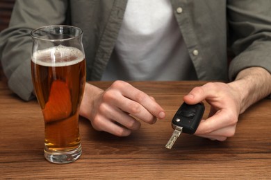 Man holding car key at table with glass of alcoholic drink, closeup. Don't drink and drive concept