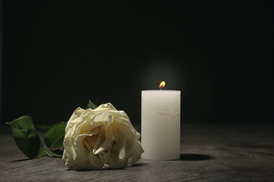 Photo of Beautiful white rose and candle on table against black background. Funeral symbol