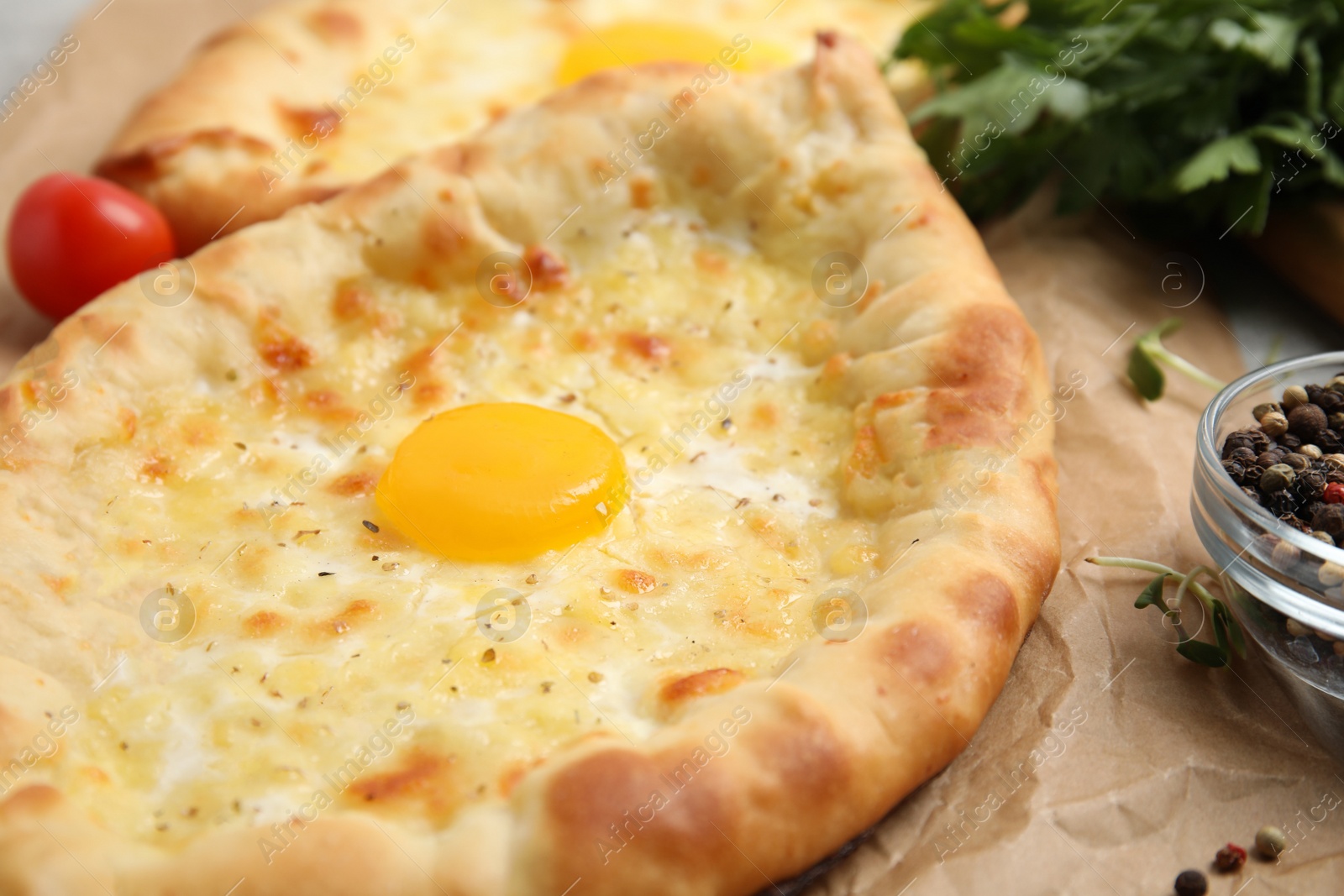 Photo of Fresh delicious Adjarian khachapuri on parchment, closeup