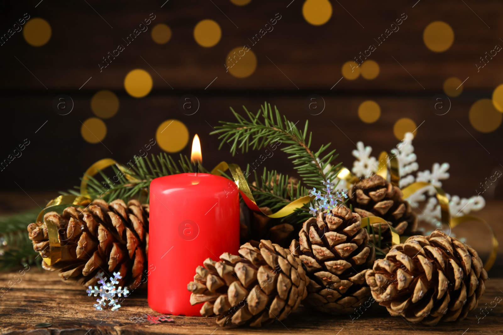 Photo of Burning candle, pine cones and fir tree branches on wooden table against blurred festive lights. Christmas eve