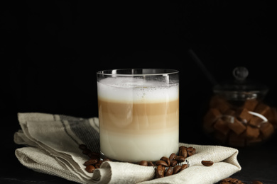 Delicious latte macchiato and coffee beans on table against black background