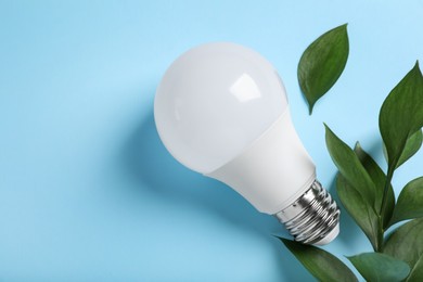 Photo of Light bulb and branch with green leaves on color background, flat lay. Space for text