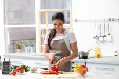 Young woman cutting vegetables for soup at table in kitchen