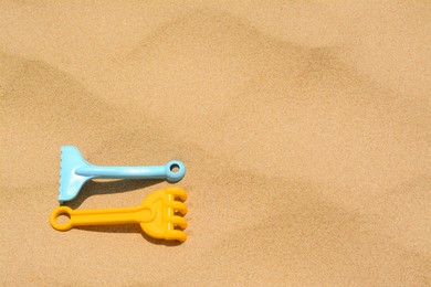 Photo of Colorful plastic rakes on sand, space for text. Beach toys