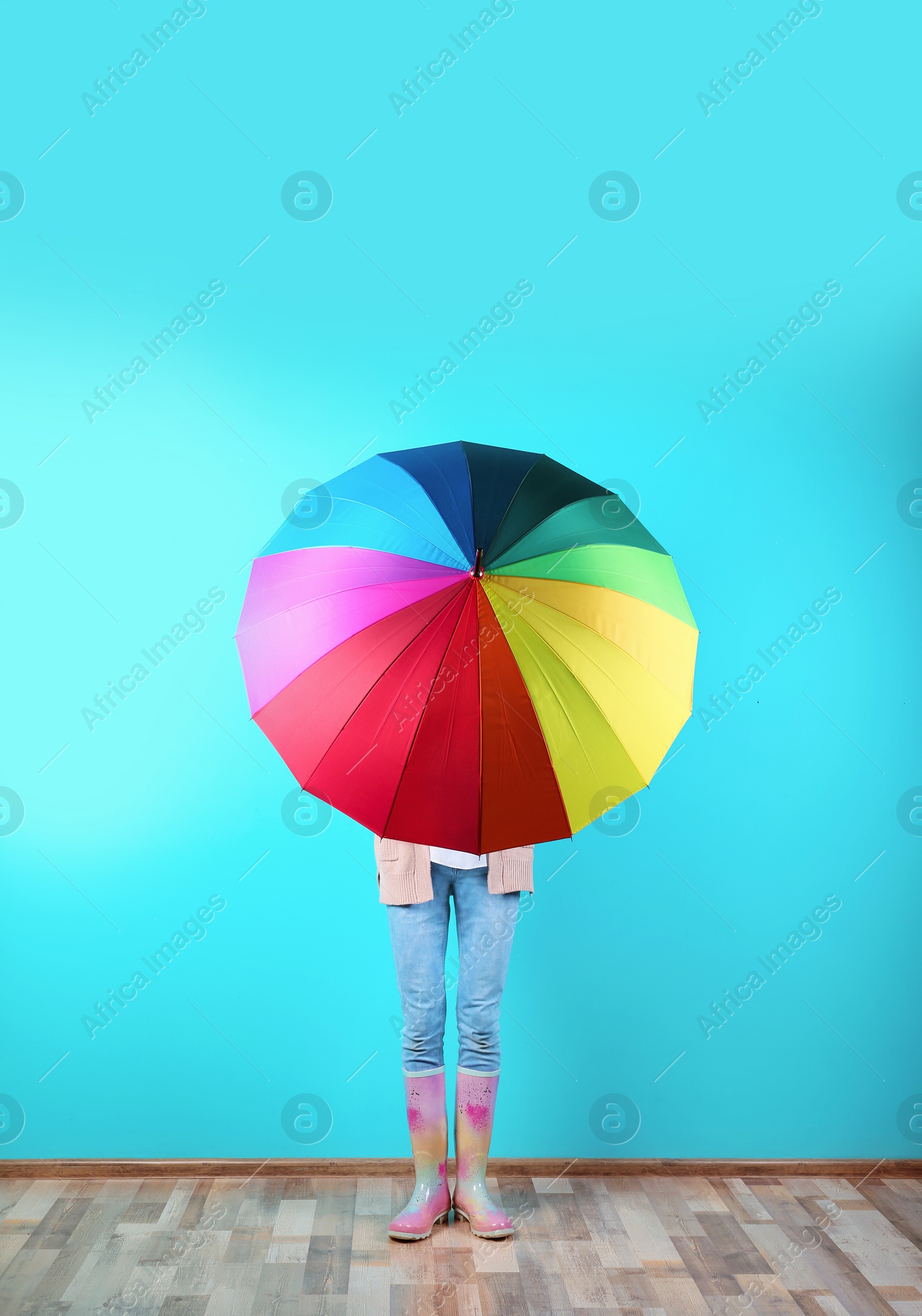 Photo of Woman hiding behind rainbow umbrella near color wall