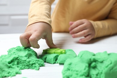 Little child playing with kinetic sand at white table, closeup