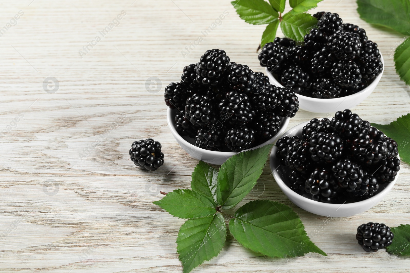 Photo of Ripe blackberries and green leaves on white wooden table, space for text