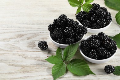 Ripe blackberries and green leaves on white wooden table, space for text