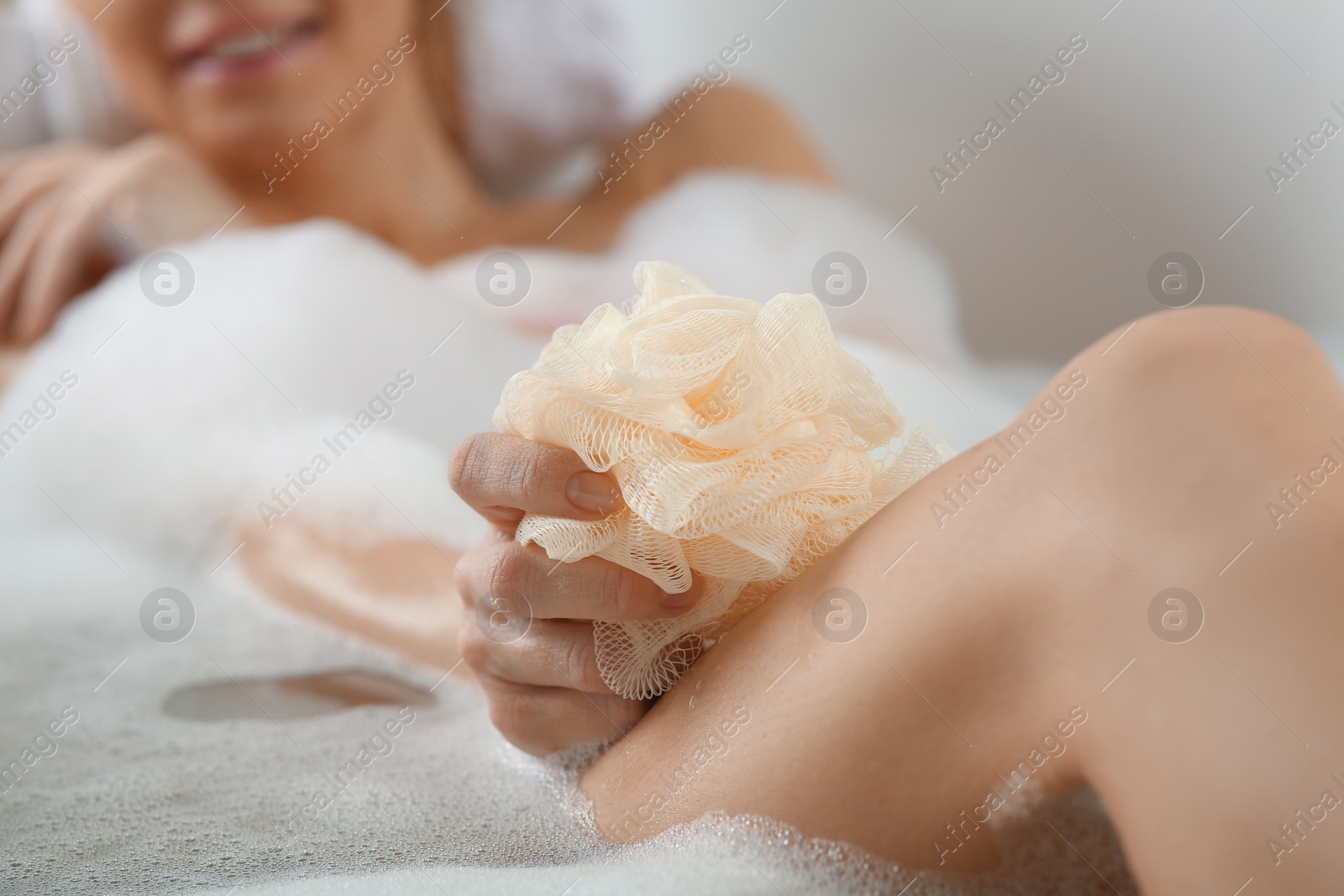 Photo of Closeup of woman taking bath, focus on hand with mesh sponge