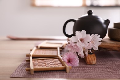 Photo of Pot, sakura flowers and bamboo coasters for traditional tea ceremony on table