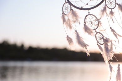 Photo of Beautiful handmade dream catcher near river on sunny day. Space for text