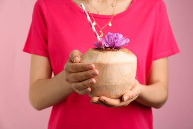 Photo of Woman holding fresh young coconut with straw on pink background, closeup