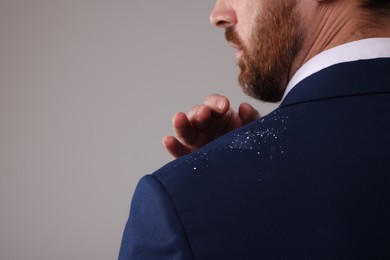 Photo of Man swiping dandruff of his suit against grey background, closeup. Space for text