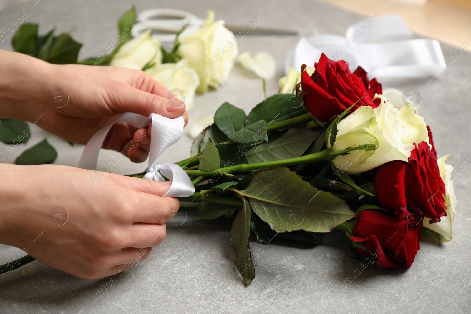 Photo of Woman making luxury bouquet of fresh roses at grey table, closeup