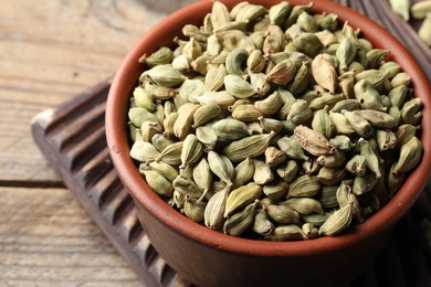 Photo of Bowl of dry cardamom pods on wooden table, closeup