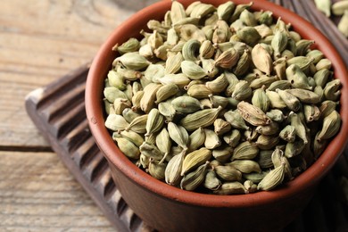 Bowl of dry cardamom pods on wooden table, closeup