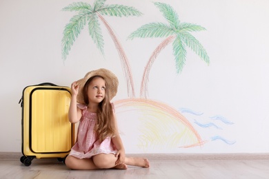 Photo of Adorable little child playing traveler with suitcase indoors