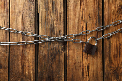 Photo of Steel padlock and chains on wooden background, flat lay. Safety concept