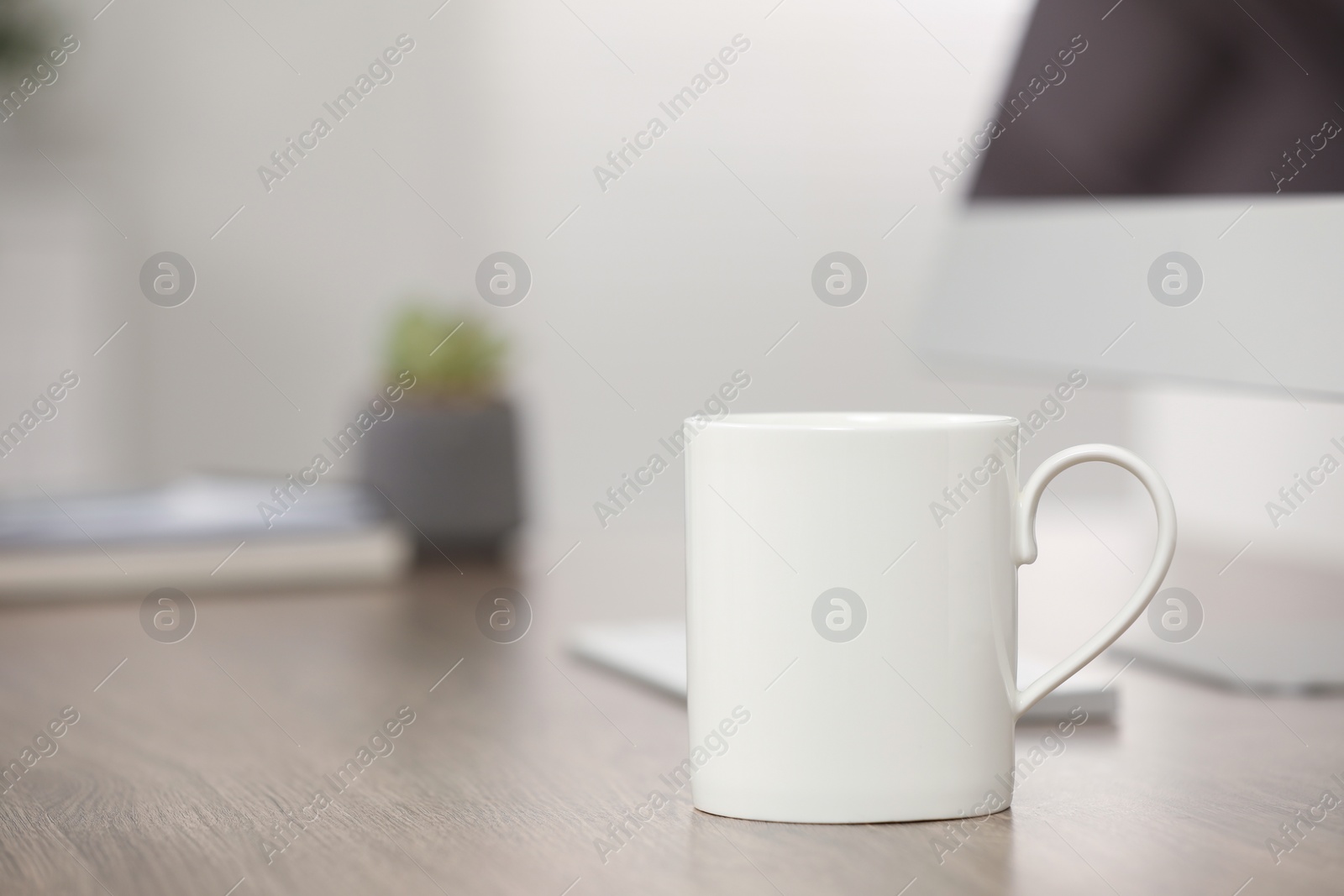 Photo of White ceramic mug and computer on wooden table at workplace. Space for text