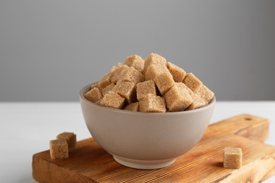 Photo of Brown sugar cubes in bowl on white table, closeup