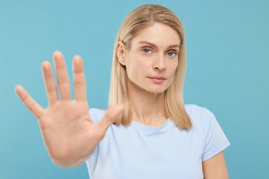 Woman showing stop gesture on light blue background