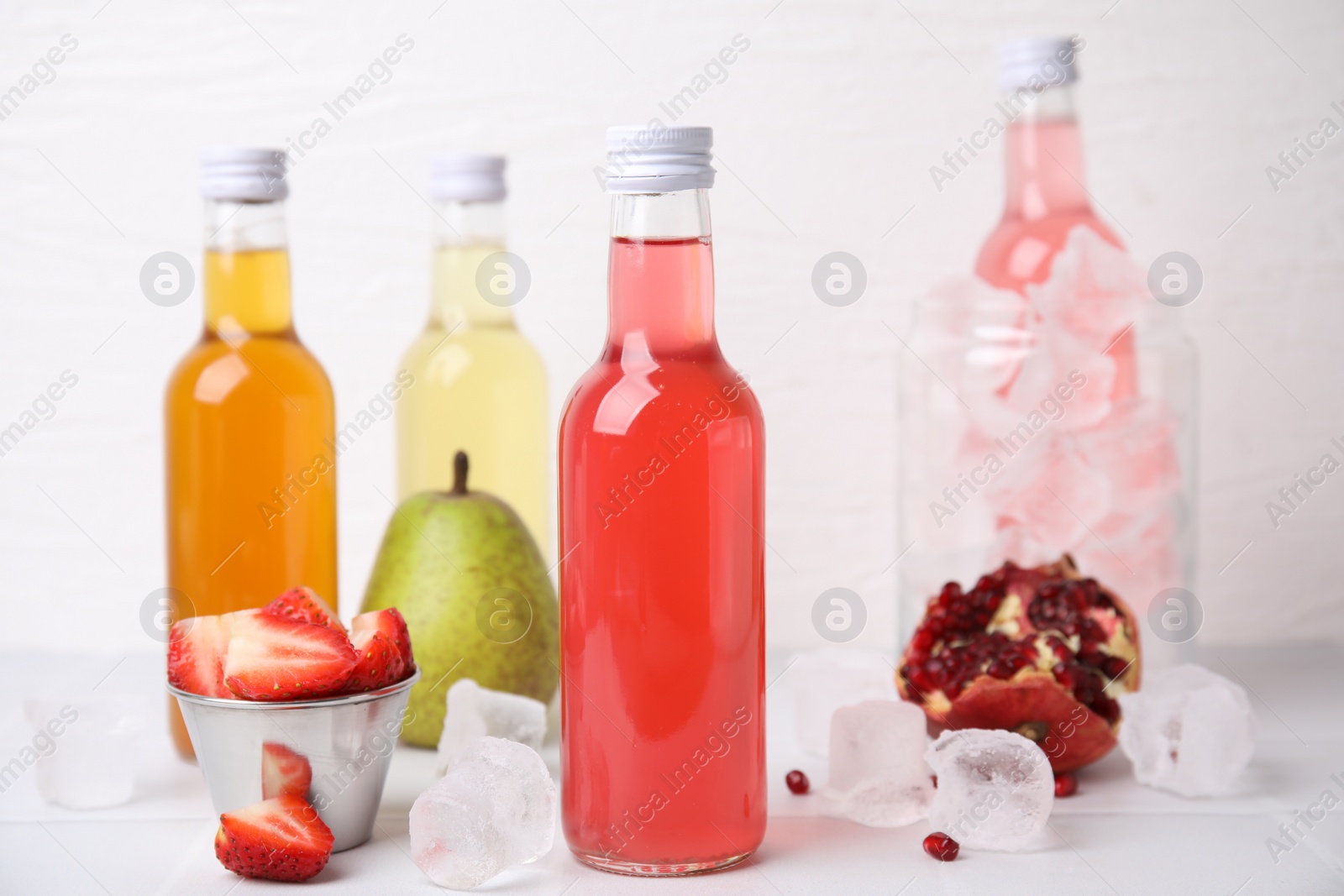 Photo of Tasty kombucha in glass bottles, fresh fruits and ice on white table