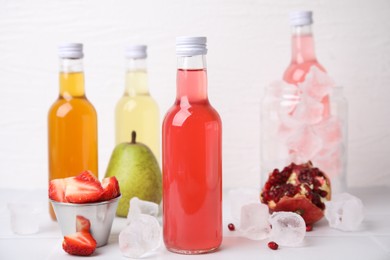 Tasty kombucha in glass bottles, fresh fruits and ice on white table