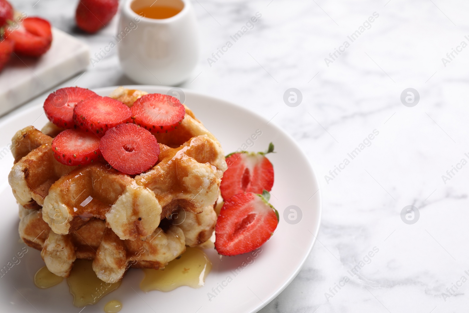 Photo of Delicious Belgian waffles with strawberries and honey on white marble table, closeup. Space for text