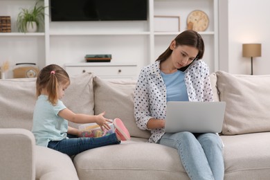 Little daughter playing while her mother working remotely on sofa at home