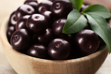 Photo of Tasty acai berries and green leaves in wooden bowl, closeup