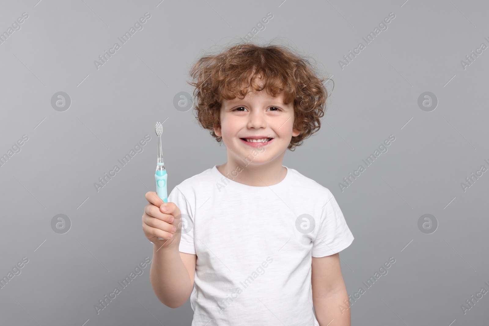 Photo of Cute little boy holding electric toothbrush on light grey background