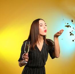 Photo of Portrait of happy woman with champagne in glass blowing off confetti on color background