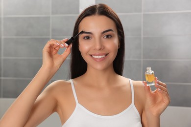 Photo of Young woman with eyelash oil in bathroom