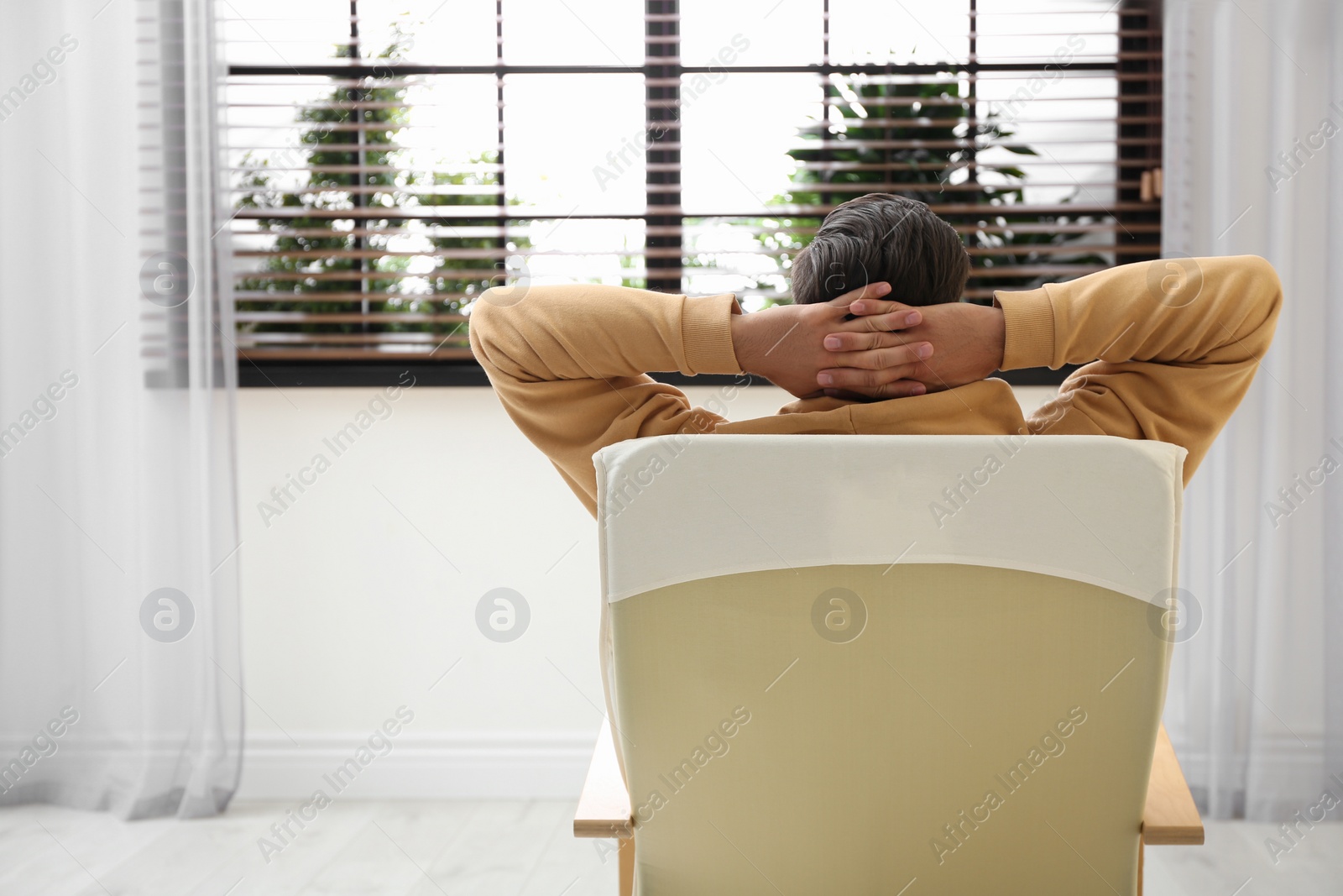 Photo of Man relaxing in armchair near window at home, back view