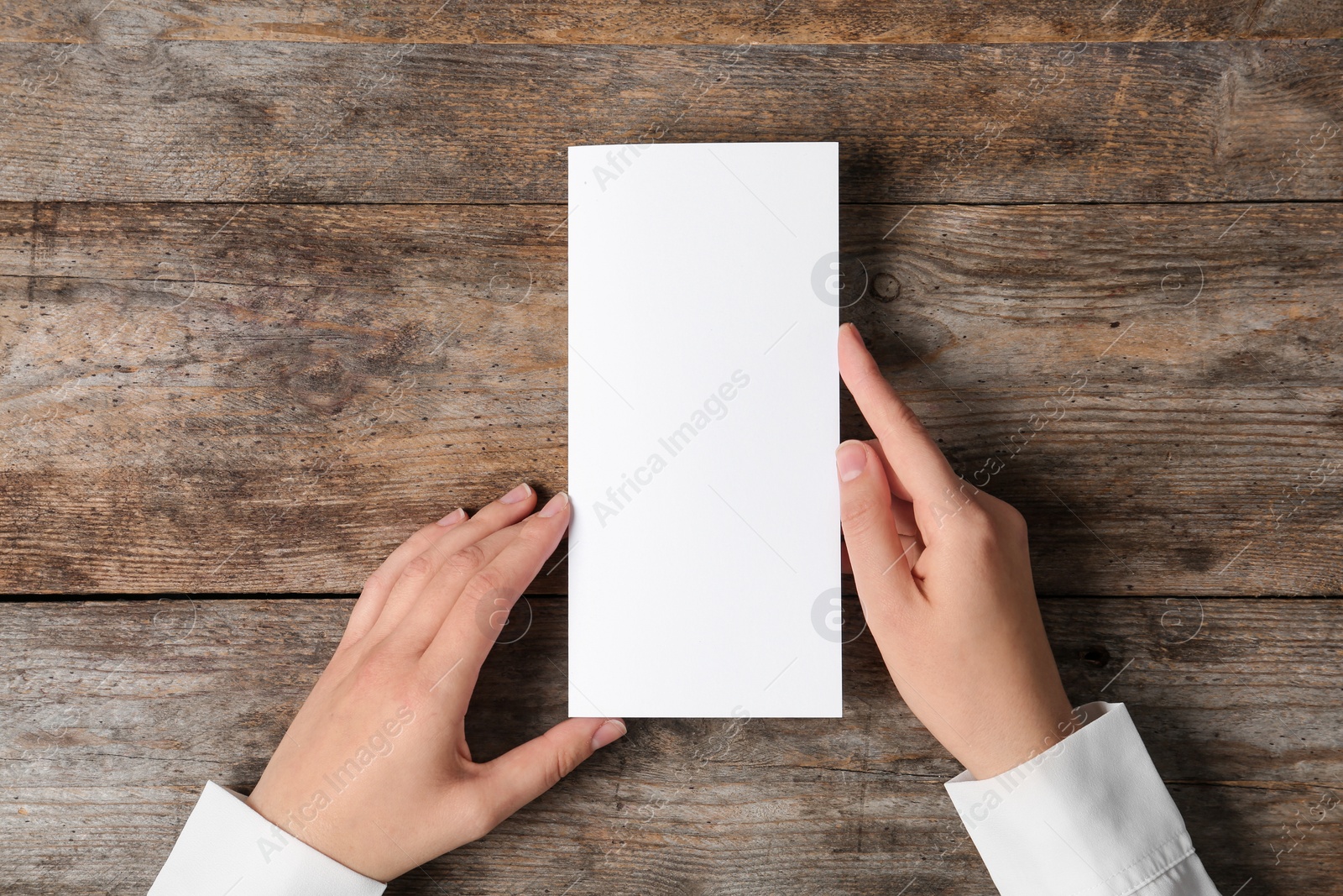 Photo of Woman holding blank brochure mock up on wooden table, top view