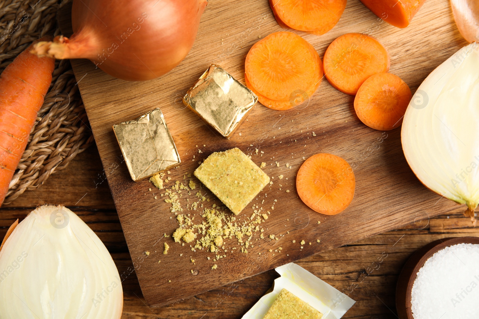 Photo of Bouillon cubes, cut carrot and onions on wooden table, flat lay