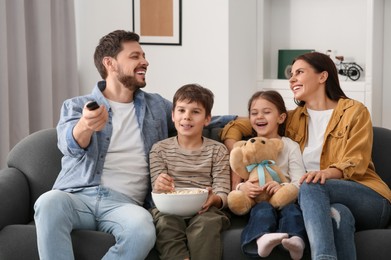 Photo of Happy family watching TV at home. Father changing channels with remote control