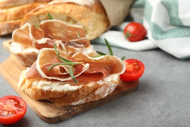 Photo of Tasty sandwiches with cured ham, tomatoes and rosemary on grey table, closeup