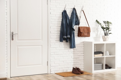 Photo of Stylish hallway interior with door, comfortable furniture and clothes on brick wall