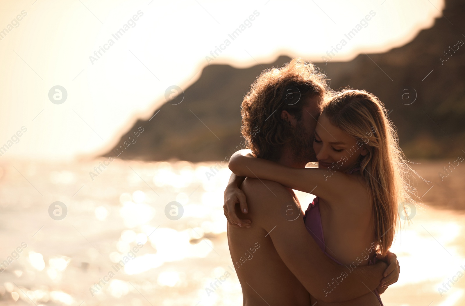 Photo of Young woman in bikini and her boyfriend on beach at sunset. Lovely couple