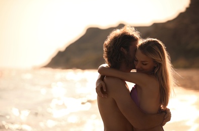 Young woman in bikini and her boyfriend on beach at sunset. Lovely couple