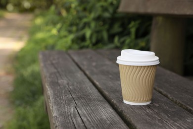 Photo of Paper cup on wooden bench outdoors, space for text. Coffee to go