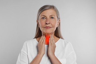Endocrine system. Senior woman doing thyroid self examination on light grey background