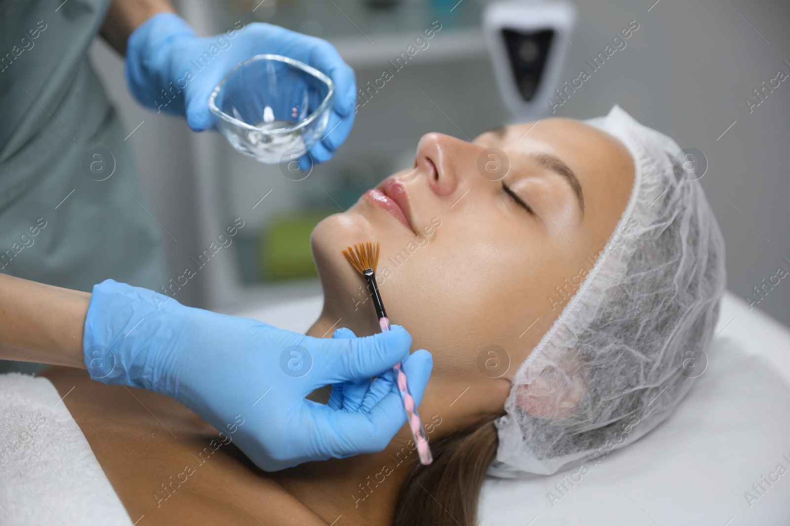 Photo of Cosmetologist applying chemical peel product on client's face in salon