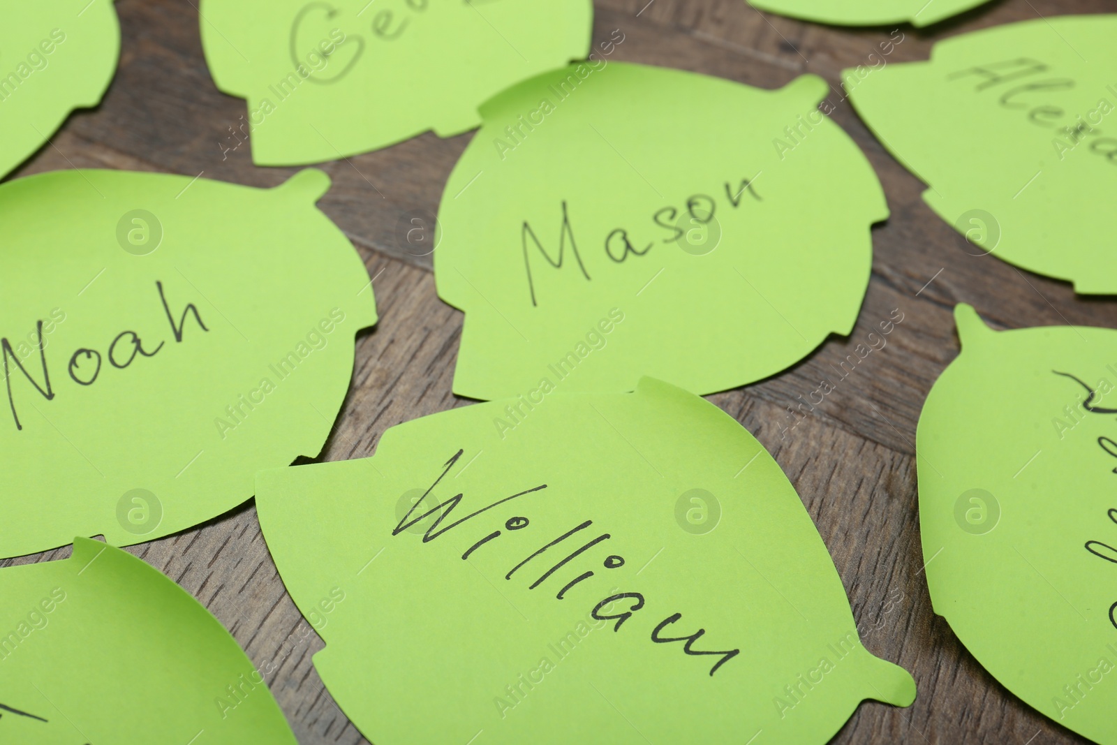 Photo of Paper stickers with different names on wooden table, closeup. Choosing baby's name