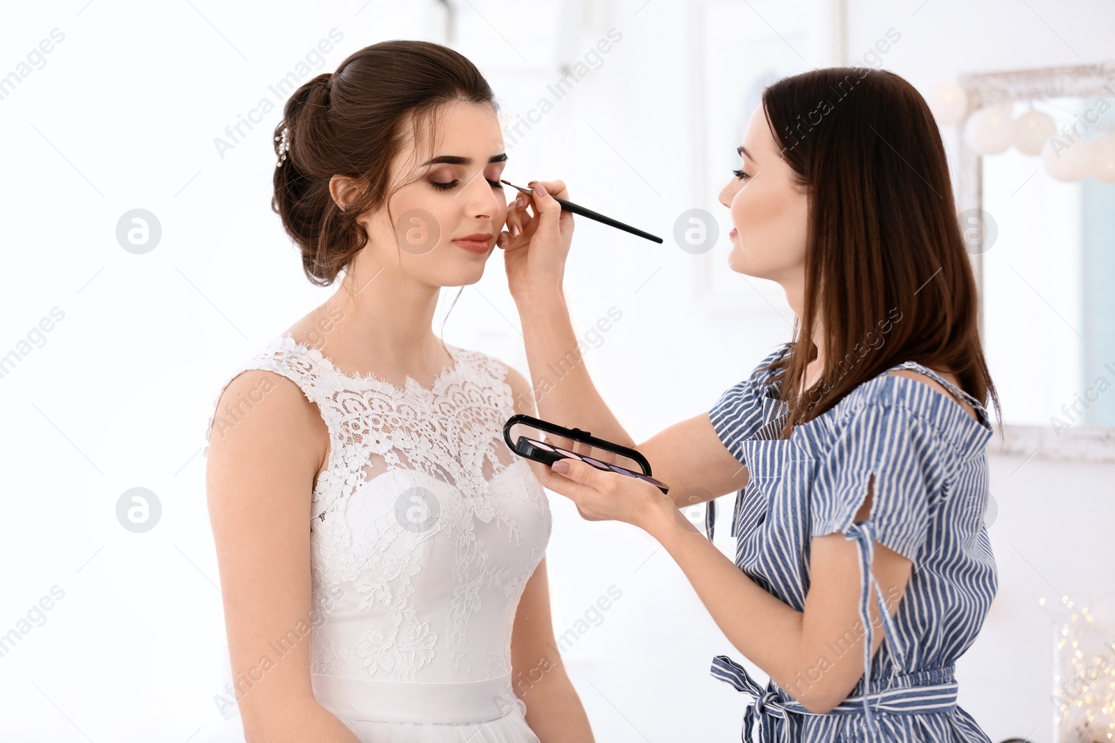 Photo of Professional makeup artist working with young woman in salon