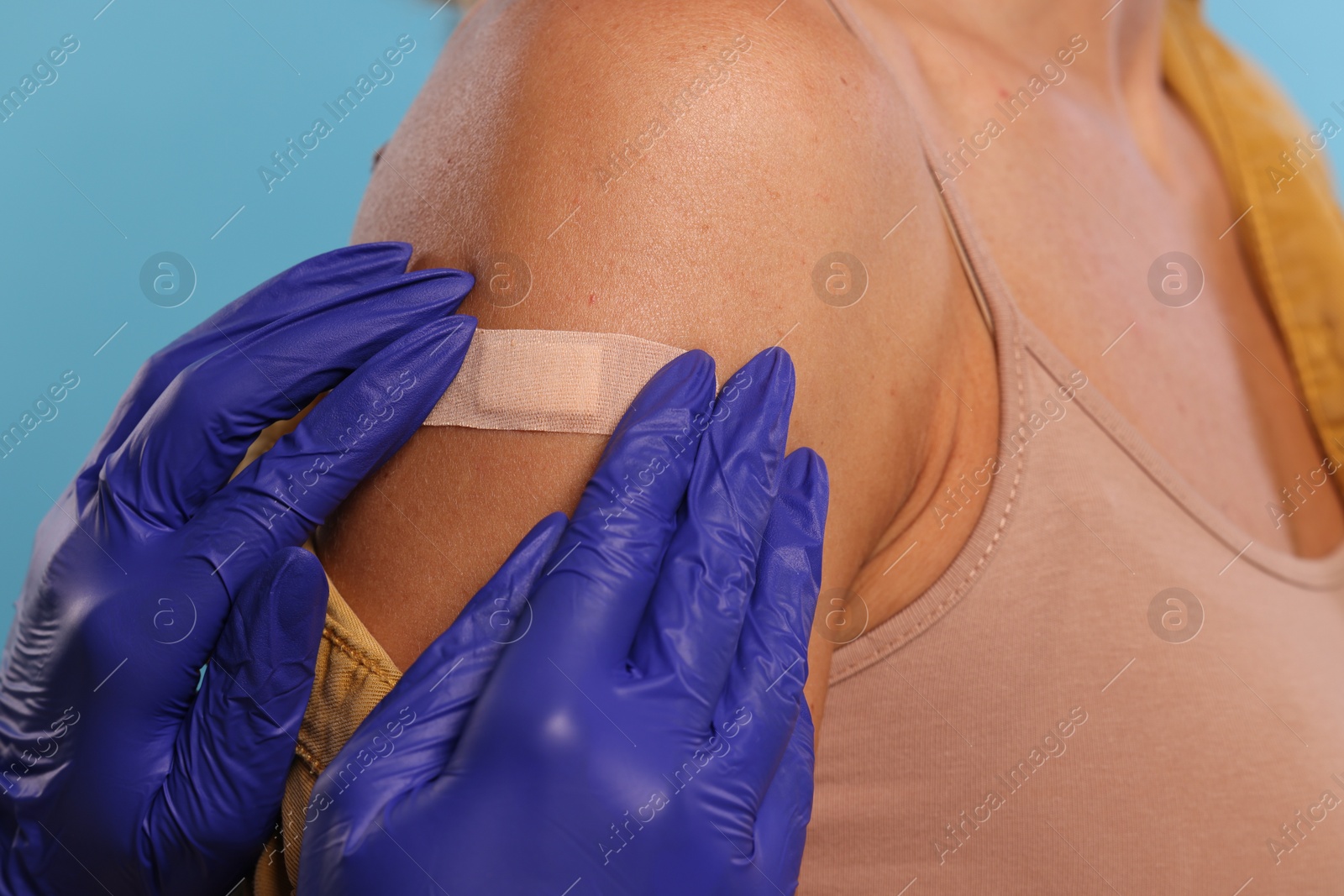 Photo of Nurse sticking adhesive bandage on woman's arm after vaccination on light blue background, closeup