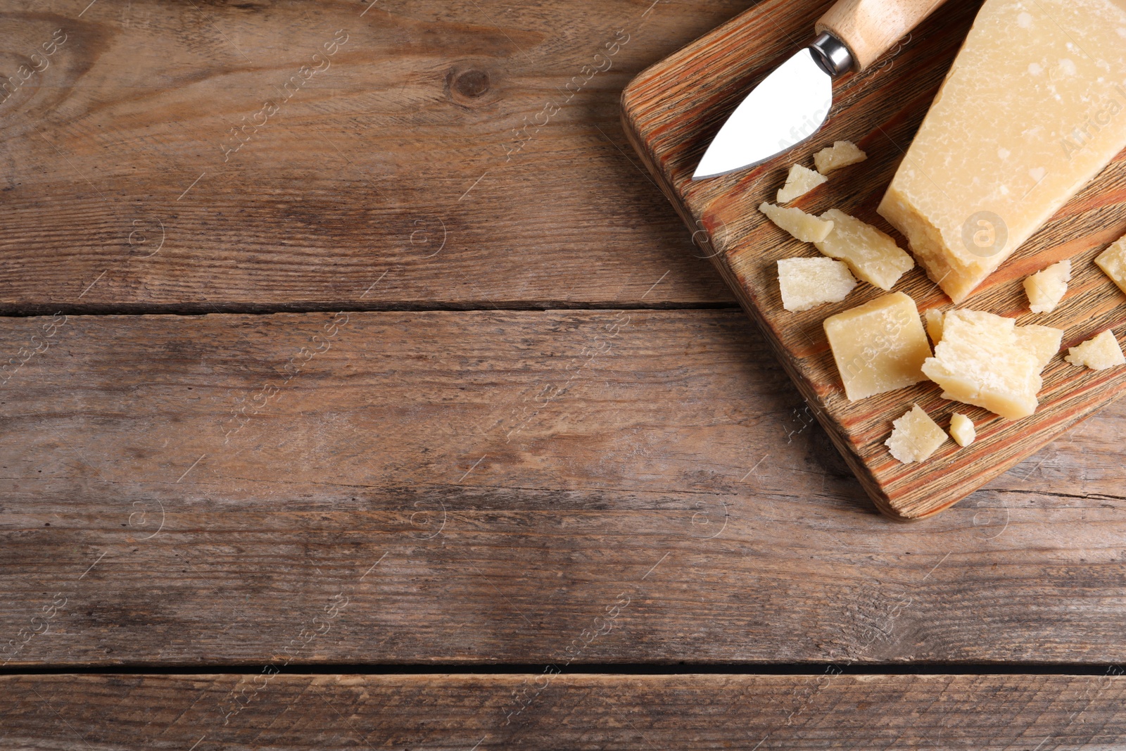 Photo of Parmesan cheese with knife on wooden table, top view. Space for text