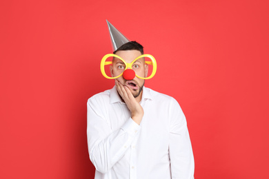 Funny man with large glasses, party hat and clown nose on red background. April fool's day
