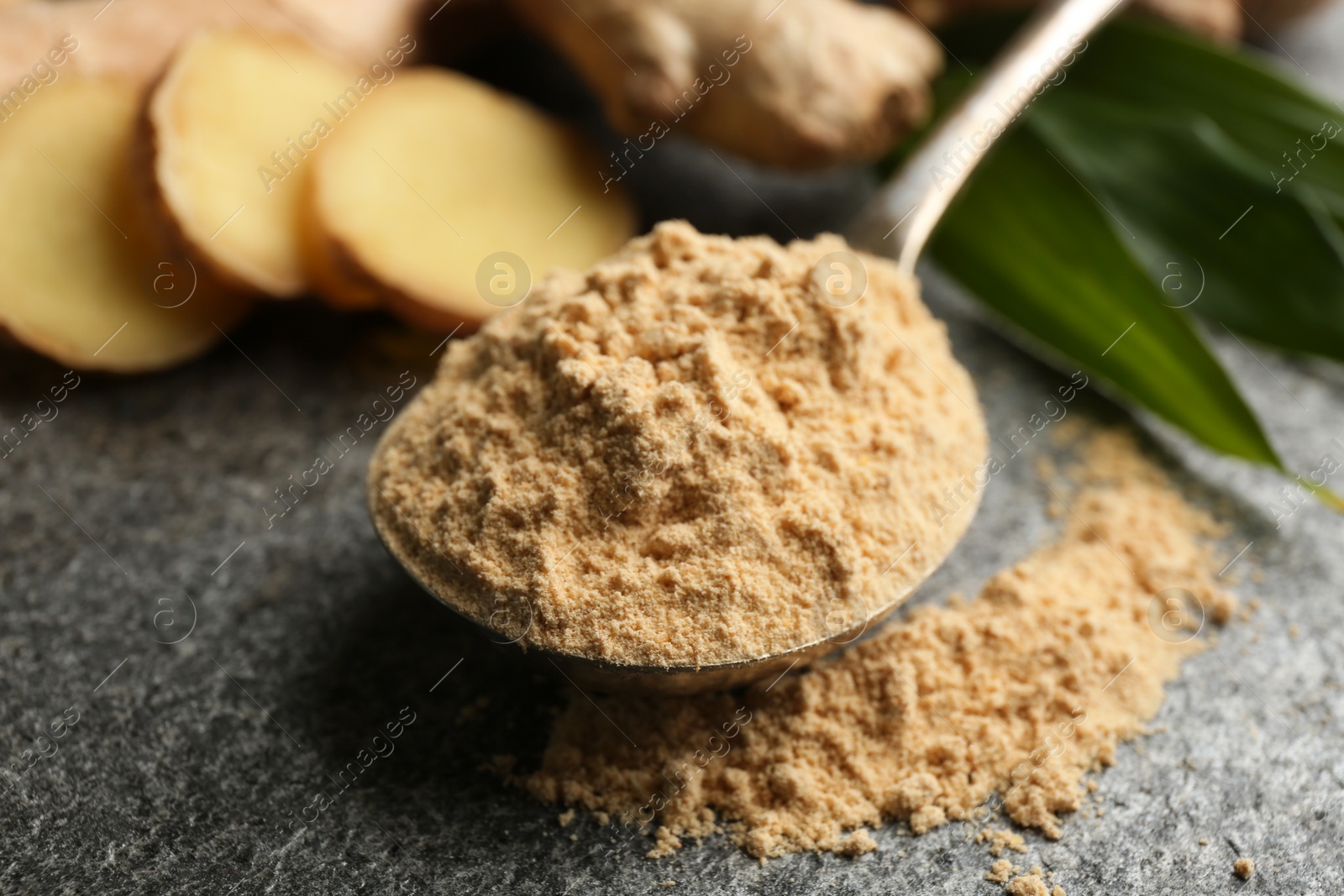 Photo of Dry ginger powder in spoon on grey table, closeup